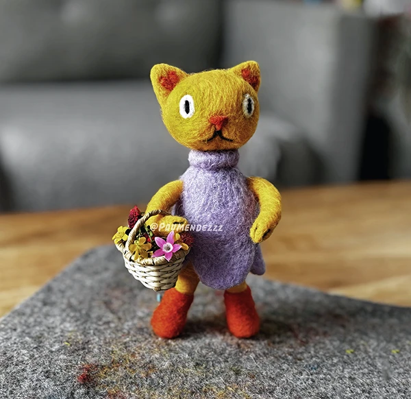 Felt figure of a yellow cat wearing a dress, holding a basket
