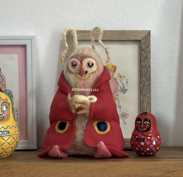 Felt figure of a moth with a red cape and big eyes